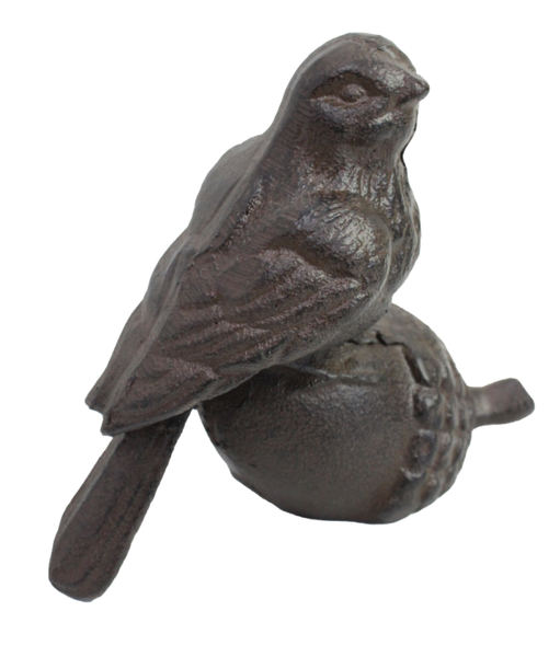 A small, dark black cast-iron figurine of a bird with textured feathers perched on top of a sculpted acorn. The figurine has a rustic, weathered appearance.