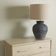 A chest of drawers with three full-width drawers. The frame and drawer faces are a distressed white wash colour, and the frame corners and drawer separators have subtle raised detailing that resembles bamboo poles. The drawers have long, recessed pull handles. Styled image with a lamp on top.