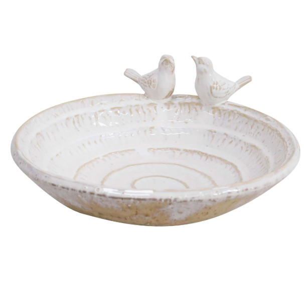 A shallow, rounded ceramic bird bath with a smooth, neutral-coloured finish. The edge of the bath is slightly curved, with two small, sculpted birds perched on opposite sides.
