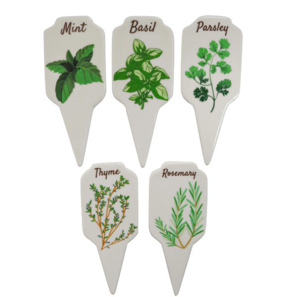 A set of five white ceramic garden stakes with pointed ends. Each stake is labelled with a different herb name (Basil, Mint, Parsley, Thyme, Rosemary) in green lettering and has a simple green botanical illustration.