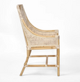 A dining chair with a frame made of light-coloured bamboo. The backrest is tall with a woven rattan insert and an arched top detail. The seat is a light, natural-coloured fabric cushion. The chair has armrests and a high back. Side view