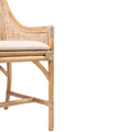 A dining chair with a frame made of light-coloured bamboo. The backrest is tall with a woven rattan insert and an arched top detail. The seat is a light, natural-coloured fabric cushion. The chair has armrests and a high back. Inner armrest detail.