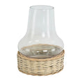 A clear glass hurricane lamp with a wide base, nestled into a woven natural wicker basket-like stand. The glass chimney is a classic, slightly flared shape, and the wicker base is a light, natural tone.