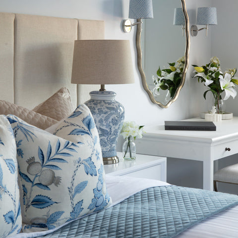 Hamptons style lampshade in soft blue and white, styled beside a ceramic table lamp in a calm coastal bedroom setting.