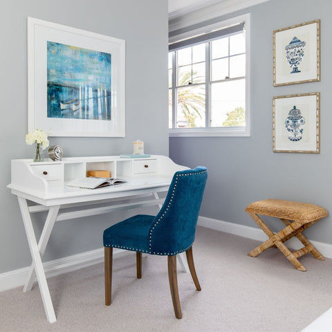 Abstract blue and white framed artwork styled above a white writing desk in a calm Hamptons-inspired home office.