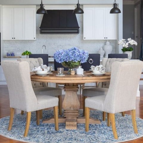 Coastal dining room with round timber dining table, upholstered chairs, blue rug and hydrangea styling