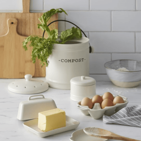 Ceramic kitchen compost bin styled on a white kitchen benchtop with timber chopping boards and fresh herbs