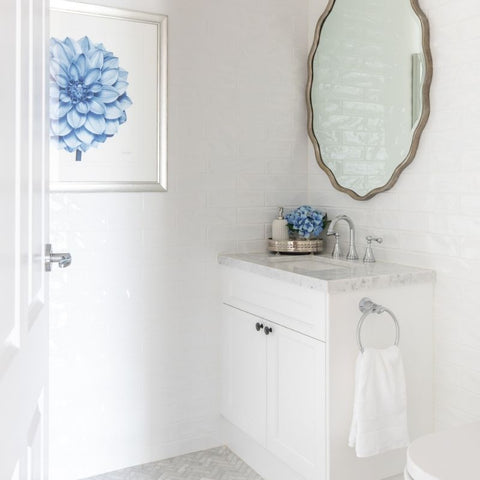 Scalloped edge wall mirror with a soft antique finish styled above a white bathroom vanity, creating an elegant Hamptons-style bathroom with coastal blue accents and classic detailing.