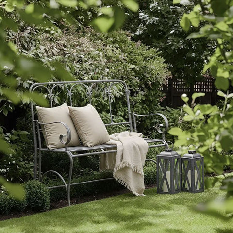 Outdoor metal garden bench with neutral cushions styled with lanterns in a lush Hamptons style garden setting
