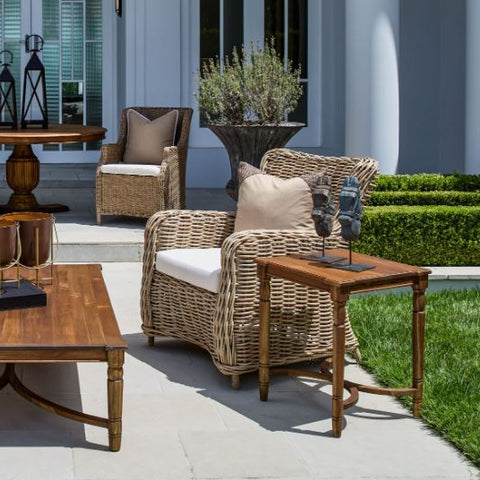 Wicker outdoor armchairs with neutral cushions styled on a Hamptons patio with timber side table and garden setting