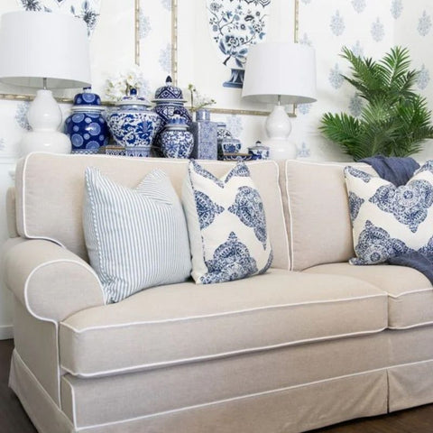 Hamptons style beige sofa styled with blue patterned cushions, white table lamps and blue and white ceramics in a coastal living room