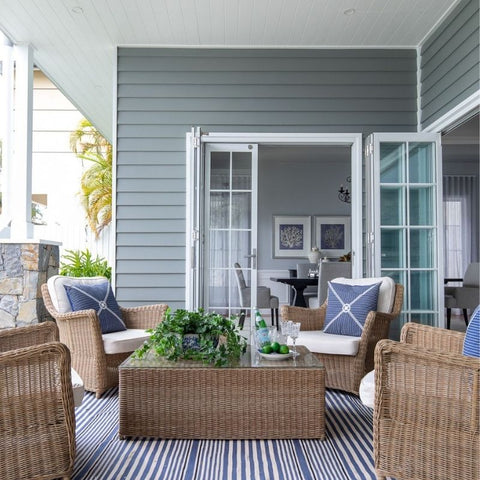 Coastal outdoor lounge styled with woven seating and soft blue and white cushions on a striped rug.