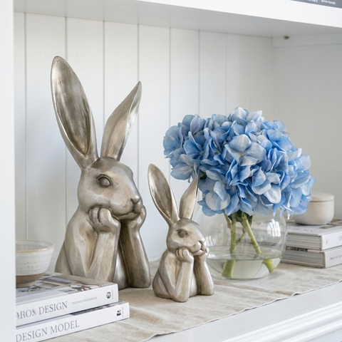 Champagne-finished hare sculptures styled on a shelf with blue hydrangeas and books in a calm Hamptons interior.