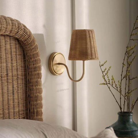 Rattan shade interior wall sconce with brass arm styled beside a woven headboard in a calm coastal bedroom.