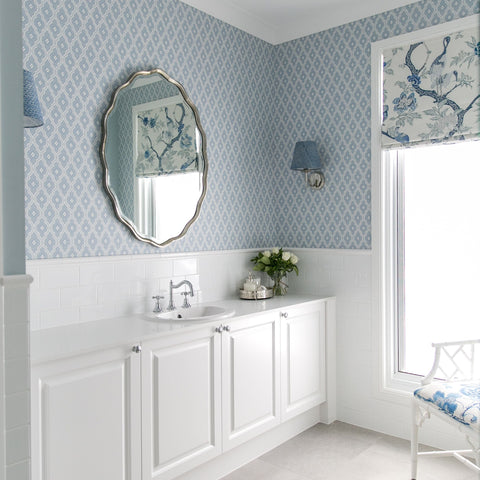 Hamptons-style bathroom with white cabinetry, patterned blue wallpaper, oval mirror and classic chrome fixtures.