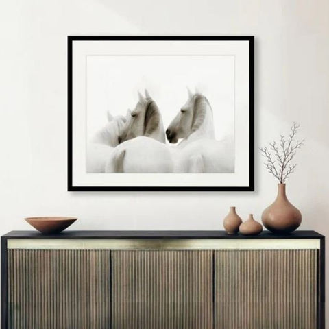 Framed animal art print featuring white horses above a console table in a calm neutral interior setting