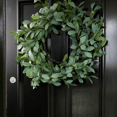 Green artificial eucalyptus wreath hanging on black front door, styled in a natural coastal Christmas aesthetic