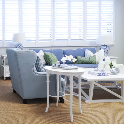 Hamptons-style living room with white side table, blue upholstered seating, natural rug and relaxed coastal styling.