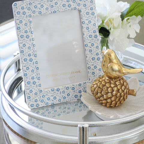 Blue and white ceramic photo frame styled on a mirrored tray with white flowers and gold decorative accents in a Hamptons-style interior.