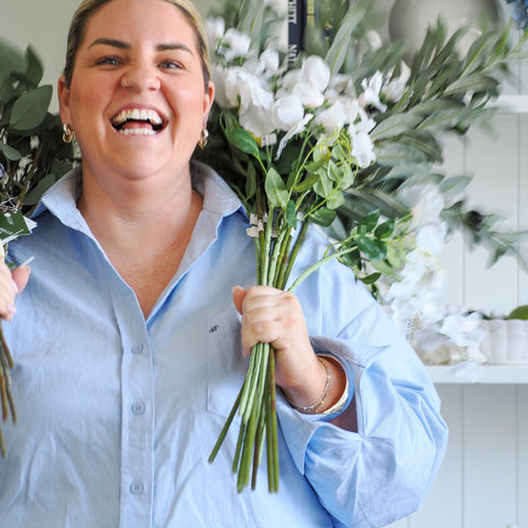 Woman holding artificial white floral stems and greenery in Hamptons style home