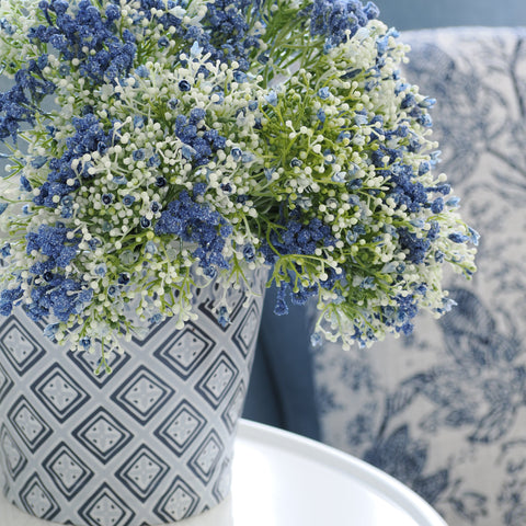 Soft blue and white artificial flowers arranged in a patterned ceramic vase, styled in a calm Hamptons living room.