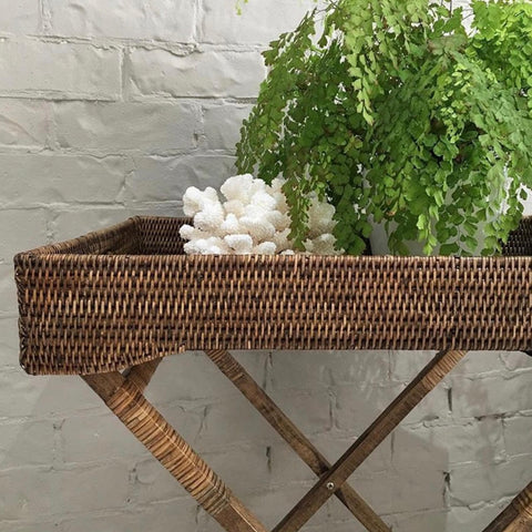 Woven rattan butlers tray styled with greenery and coral décor in a relaxed coastal interior