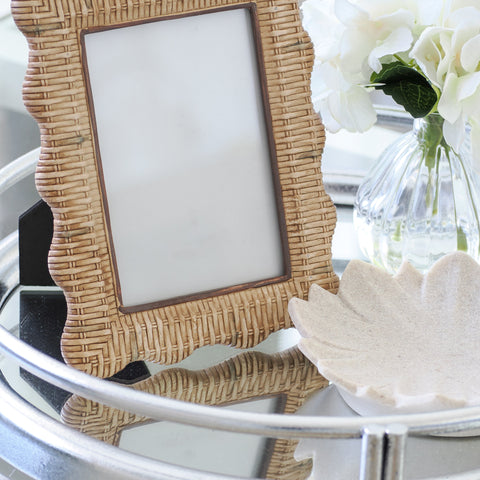 Rattan-style scalloped picture frame displayed on a mirrored tray with a ceramic dish and white flowers in a Hamptons-style setting.