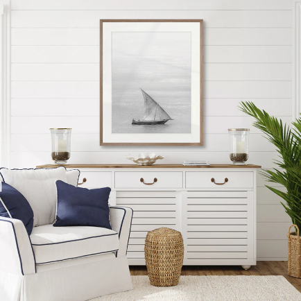 Coastal living room styled with black and white sailboat framed artwork, white console cabinet and navy cushions