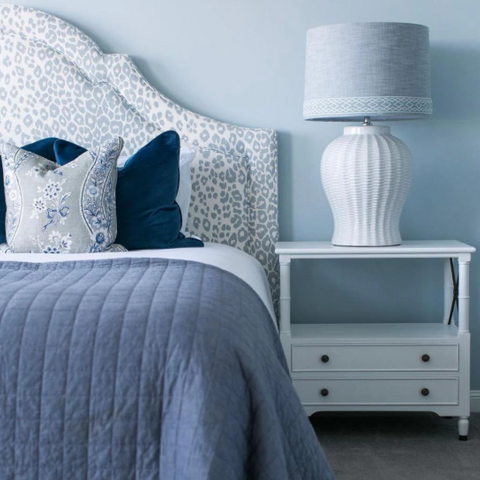 Hamptons-style bedside tables in soft white and pale timber tones, styled beside a calm coastal bedroom setting.