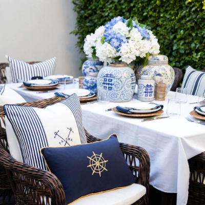 Outdoor dining setting styled with navy nautical cushions, blue striped pillows and classic coastal tableware.