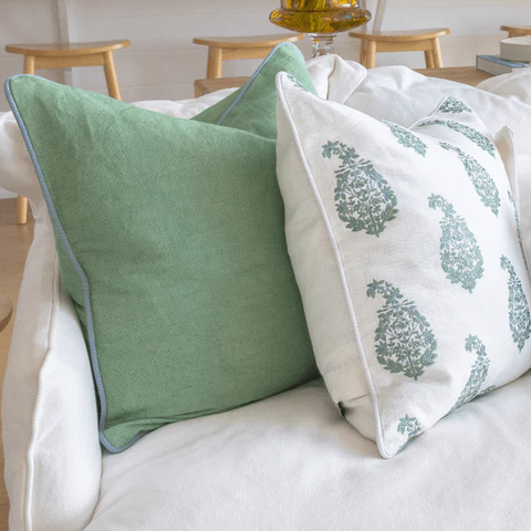 Green and white cushions styled on a sofa, featuring soft sage tones and delicate botanical print detail.