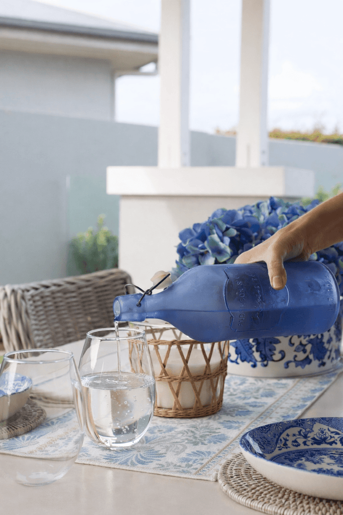 Coastal outdoor table styling with blue and white tableware, woven placemats, floral table runner and relaxed Hamptons entertaining setting