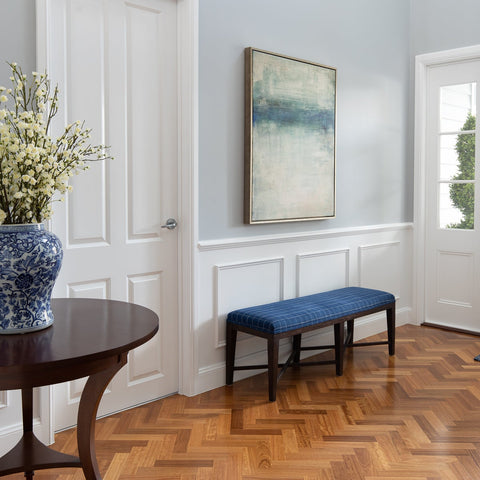 Hamptons-style entryway featuring a blue upholstered bench, console table, blue and white ceramic vase, and classic wall art.