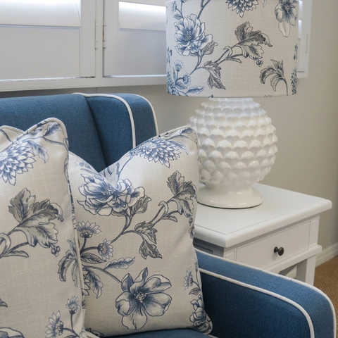 Coastal living room with blue armchair, floral cushions and white ceramic table lamp on bedside table