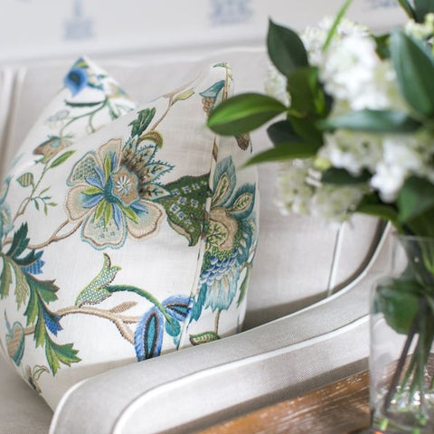 Hamptons-style floral cushion in soft blue and green tones styled on a neutral sofa with fresh white flowers.