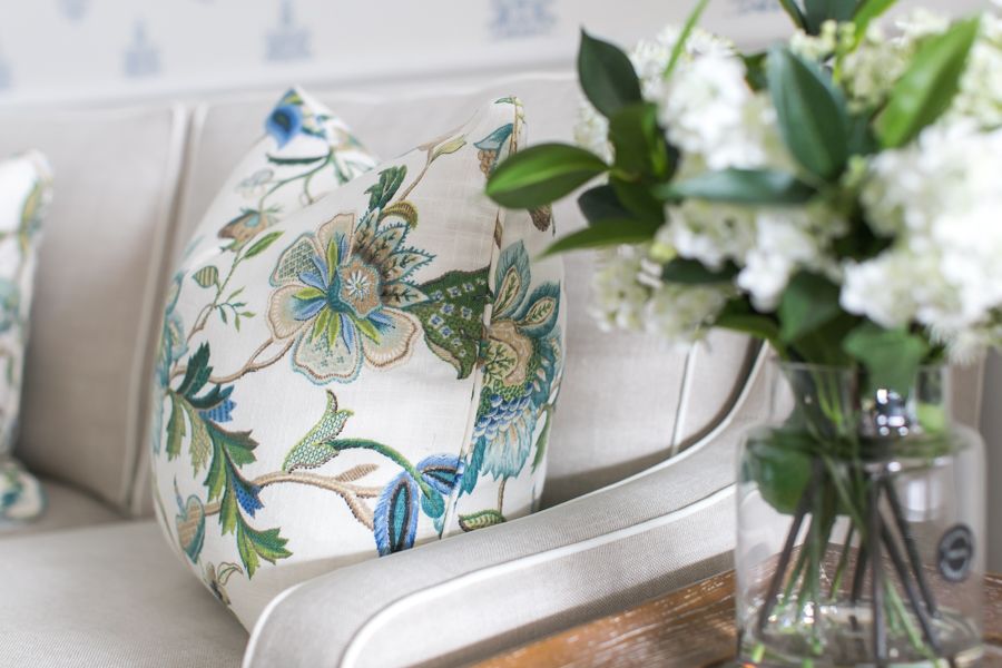 Hamptons-style floral cushion in soft blue and green tones styled on a neutral sofa with fresh white flowers.