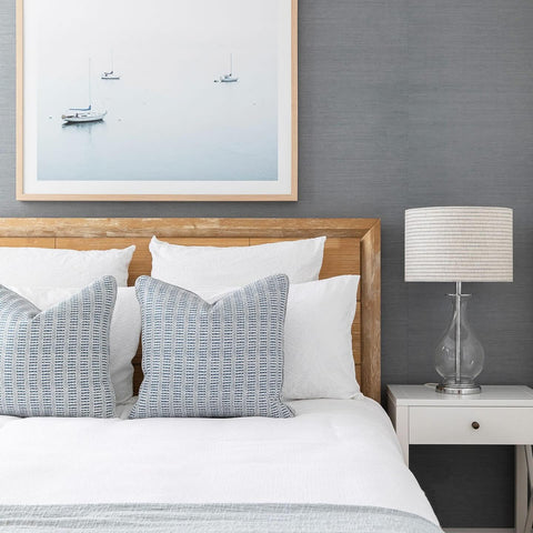 Framed coastal beach print with soft ocean tones styled above bed in a calm Hamptons style bedroom