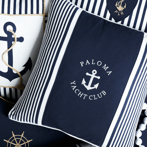 Navy blue nautical cushions with striped detailing, anchor motifs and coastal-inspired embroidery styled in a layered Hamptons interior