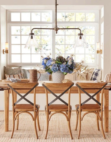 Hamptons-style dining room with a natural timber dining table, woven chairs, soft blue florals and relaxed coastal styling in a light-filled space.