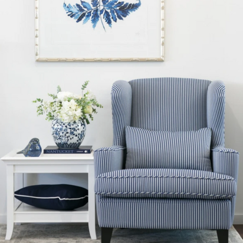 Blue striped occasional armchair styled with white side table, navy cushion and coastal artwork in a Hamptons living room