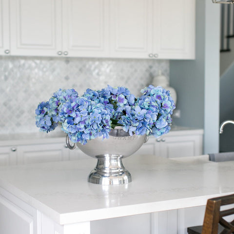 Blue hydrangea arrangement styled on a white kitchen island in a light-filled Hamptons-style interior.