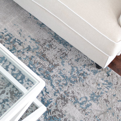 Soft grey and blue patterned rectangular rug styled beneath a white coffee table and linen sofa in a Hamptons living room.