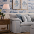 Light blue velvet cushion with soft texture and square shape on a soft blue sofa with coastal artwork above.