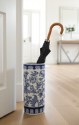 Blue and white ceramic aviary patterned umbrella stand holding a black umbrella in a hallway