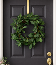 Green leafy wreath hanging on a charcoal front door with brass hardware, styled with a lantern and soft floral arrangement beside the entrance.