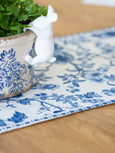 Blue and white floral table runner styled on a wooden table with a chinoiserie planter, creating a classic Hamptons-inspired tablescape.