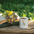 Beatrix Potter 9cm Peter Rabbit with Radish Mug filled with tea sitting beside a bunch of pretty flowers.