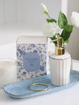 Blue and white Chinoiserie candle box styled with a white ceramic soap dispenser with gold pump, glass candle and blue decorative tray, creating an elegant Hamptons-style bathroom vignette with soft white florals.