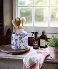 Blue floral stoneware vessel styled on a rustic kitchen bench with wooden utensils and herbs