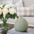 Seafoam ceramic urchin bud vase styled on coffee table books in a Hamptons-style living room with white roses, woven tray and coastal home décor.